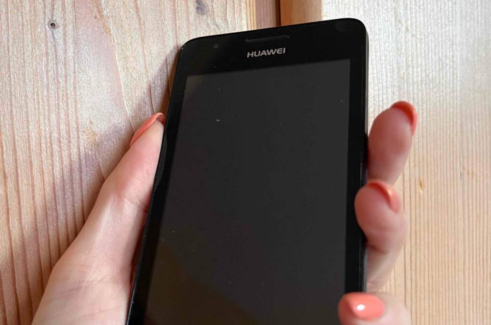 China-Handy getestet: Eine Hand hält ein China-Handy vor eine Holzoberfläche.