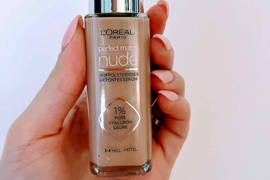 Make-up im Test: Eine Hand hält eine Flasche Make-up vor eine helle Wand