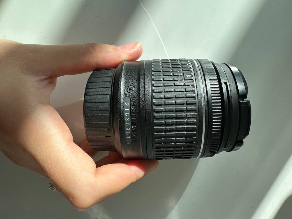 Eine Hand hält ein getestetes Objektiv für Nikon vor eine helle Wand.