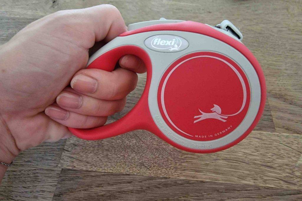 Eine Hand hält eine getestete Rollleine vor eine Holzoberfläche