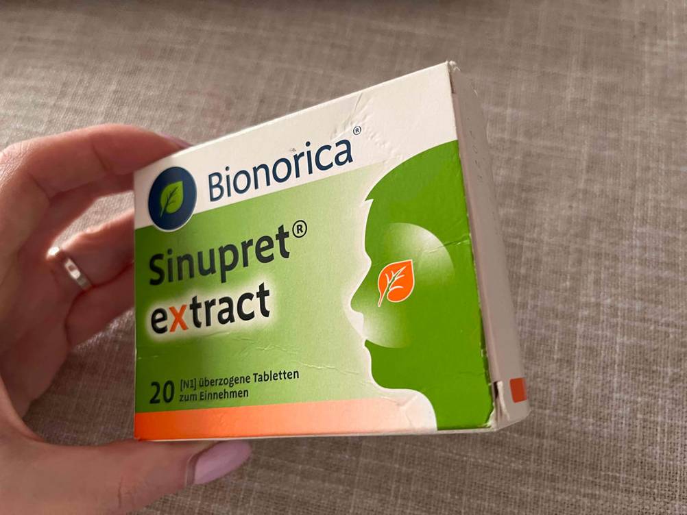 Im Test: Eine Packung Schleimlöser wird von einer Hand seitlich vor eine helle Fläche gehalten.