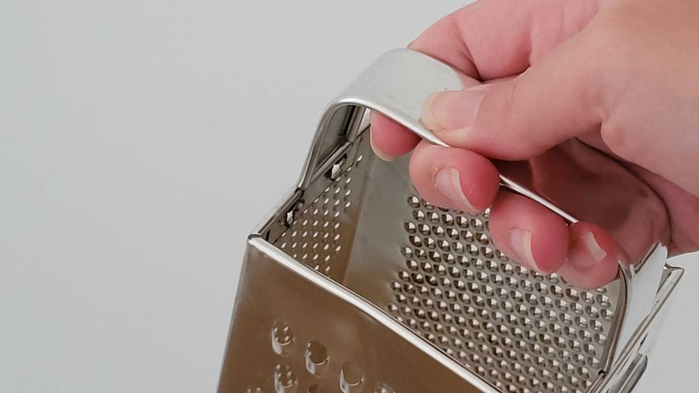 Im Test: Eine Hand hält eine Käsereibe am Griff.