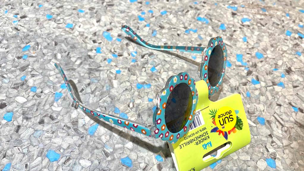Babysonnenbrille im Test: Babysonnenbrille mit Etikett auf einem graublauem Boden liegend.