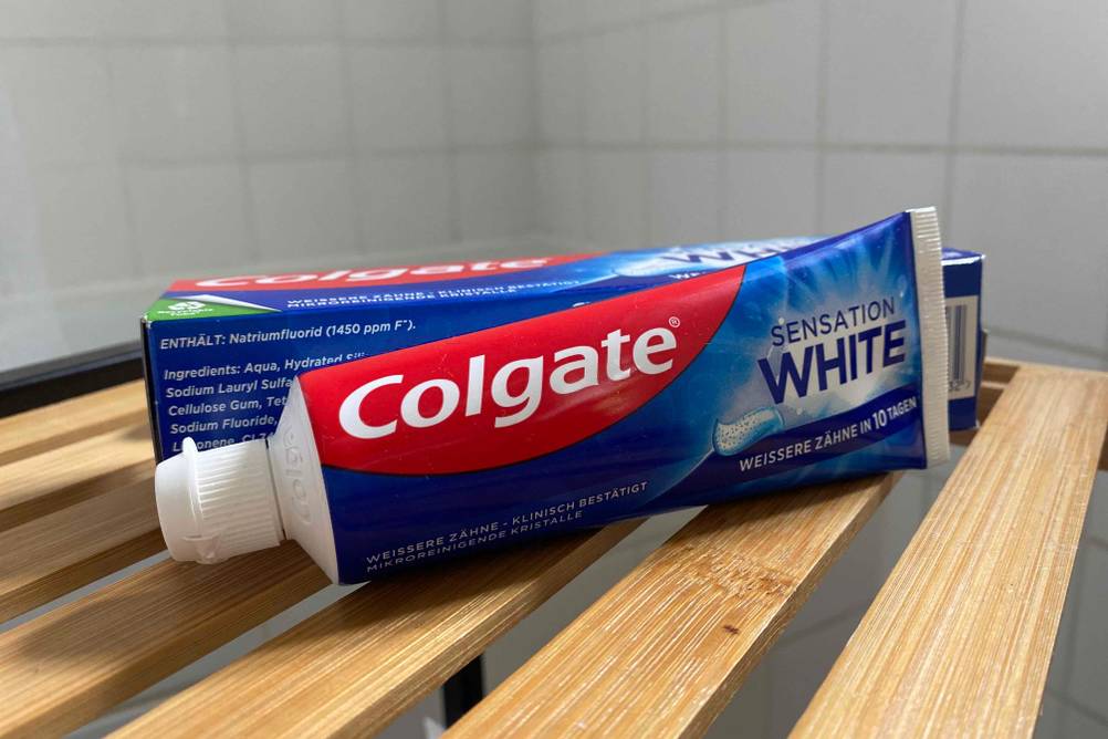 Zahnpasta gegen Zahnfleischrückgang im Test: Eine Tube Zahnpaste vor ihrer Originalverpackung auf einer Holzoberfläche