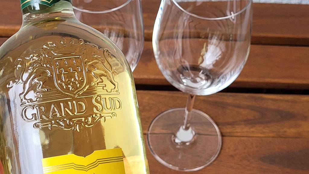 Weißwein -Test: eine Weißweinflasche wird nah an zwei Weißweingläser gehalten.