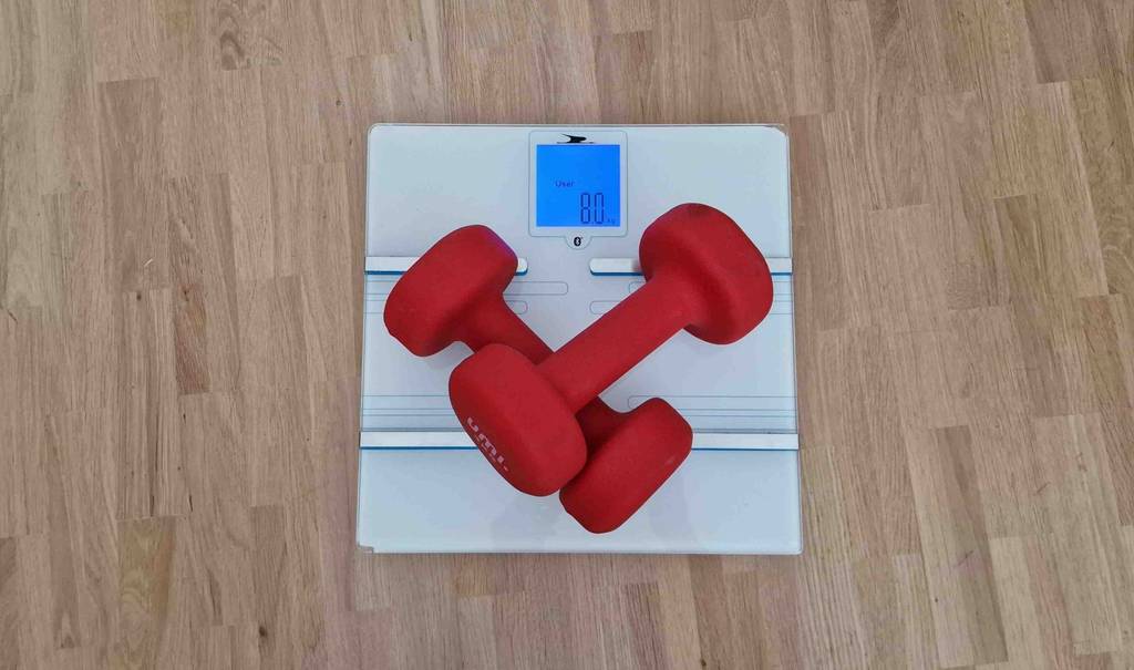 Im Test: Auf einer Körperfettwaage liegen zwei rote Hanteln.
