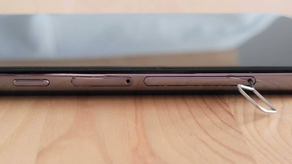 Billig-Smartphone im Test: Ein Smartphone auf der Seite liegend, mit Werkzeug zum Öffnen von SIM-Karten-Fach darin.
