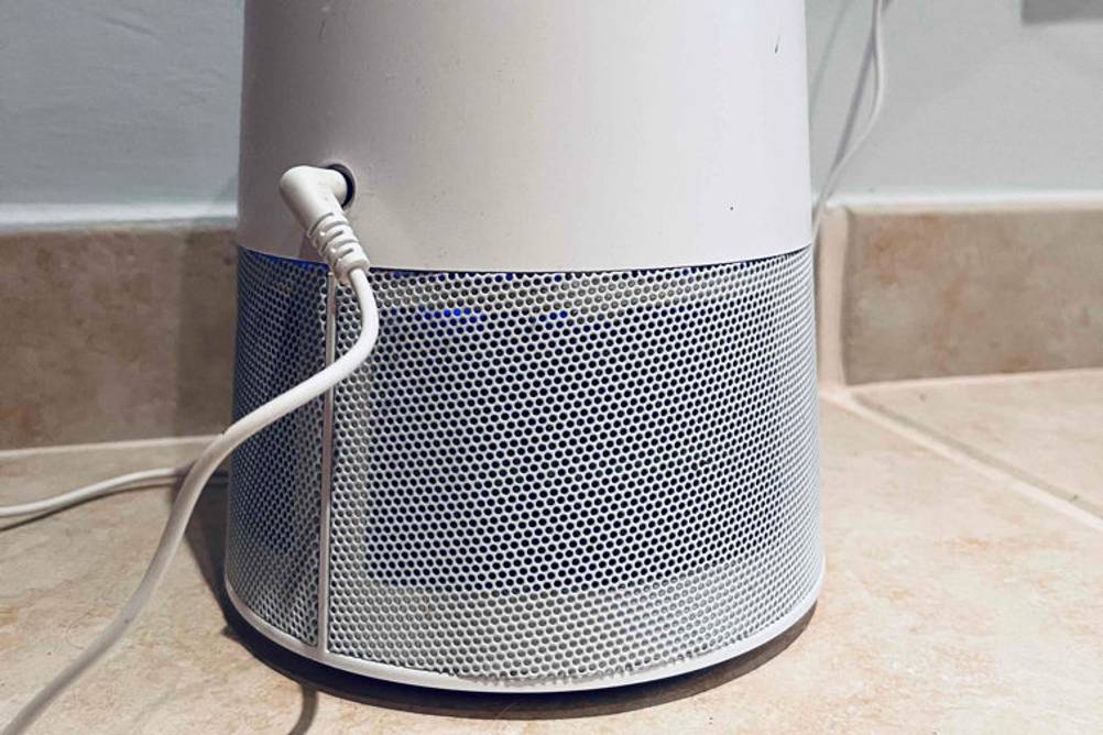 Im Test: Ein UVC-Luftreiniger steht auf einem Fließenboden vor einer hellen Wand. Ein wenig UV-Licht scheint durch das Lüftungsgitter.