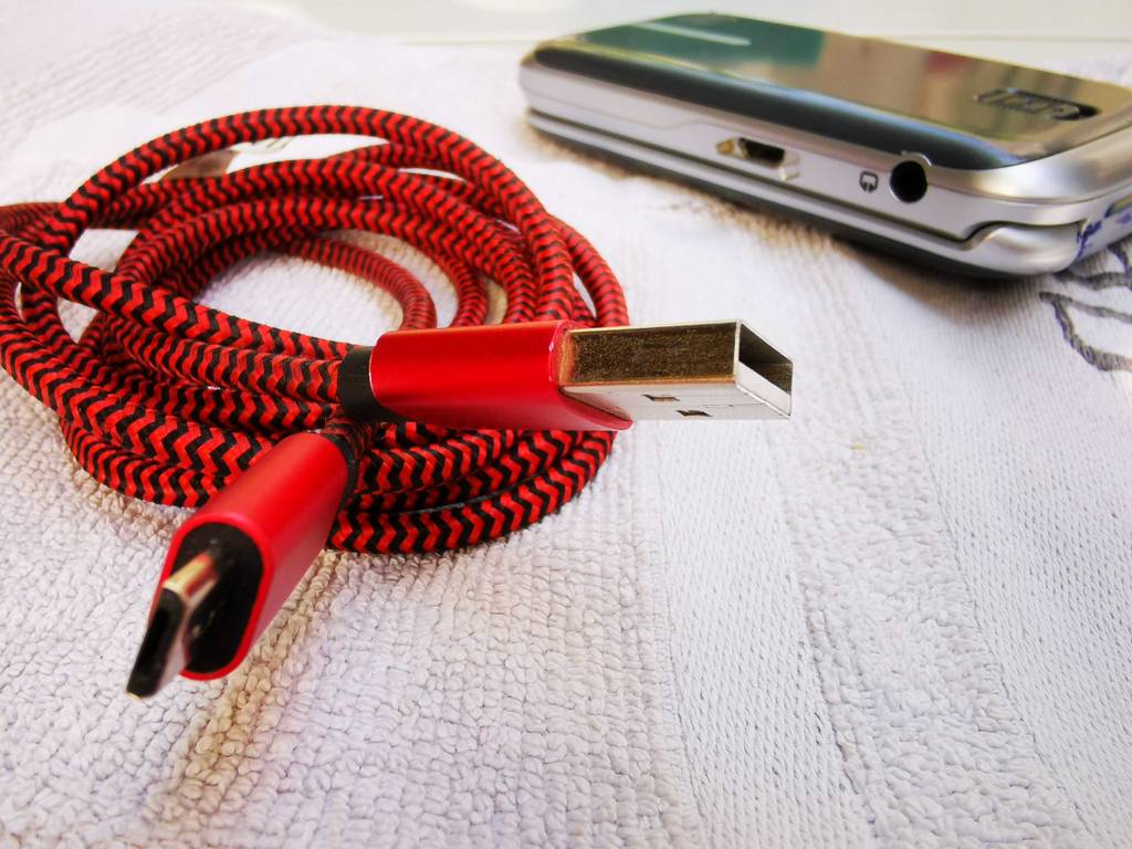 Micro-USB-Kabel im Test: Das Kabel mit der rot-schwarzen Ummantelung liegt neben einem Smartphone.