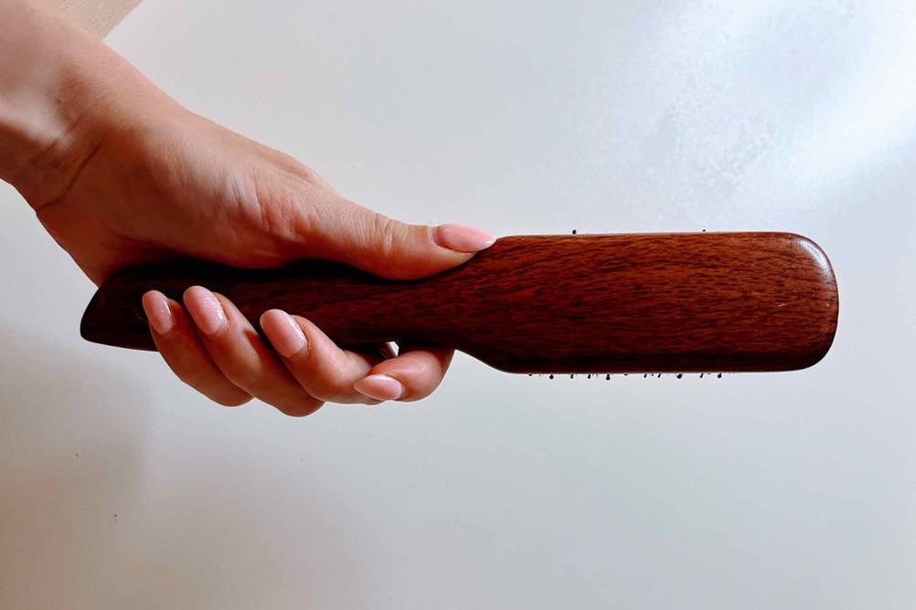 Haarbürste-Wildschweinborsten im Test: Eine Hand hält eine Bürste mit der Rückseite nach vorne vor eine helle Wand