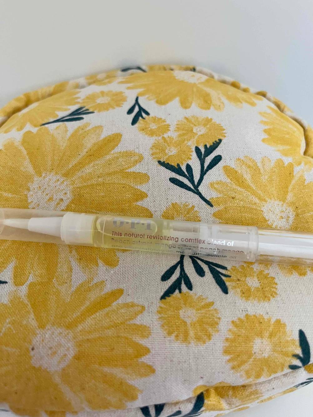 Nagelöl im Test: Ein Stift mit Nagelöl liegt auf einem geblümten Kissen