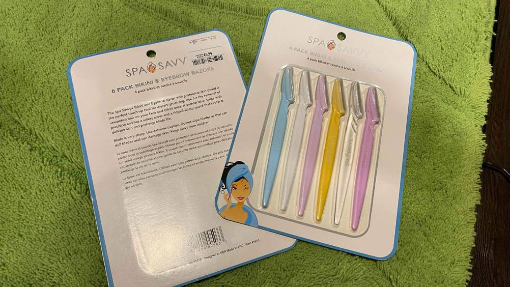 Augenbrauenrasierer getestet: zwei Verpackungen von Augenbrauenrasierern auf einem Teppich liegend - bei einem die Rückseite und dem anderen die Vorderseitee ersichtlich.