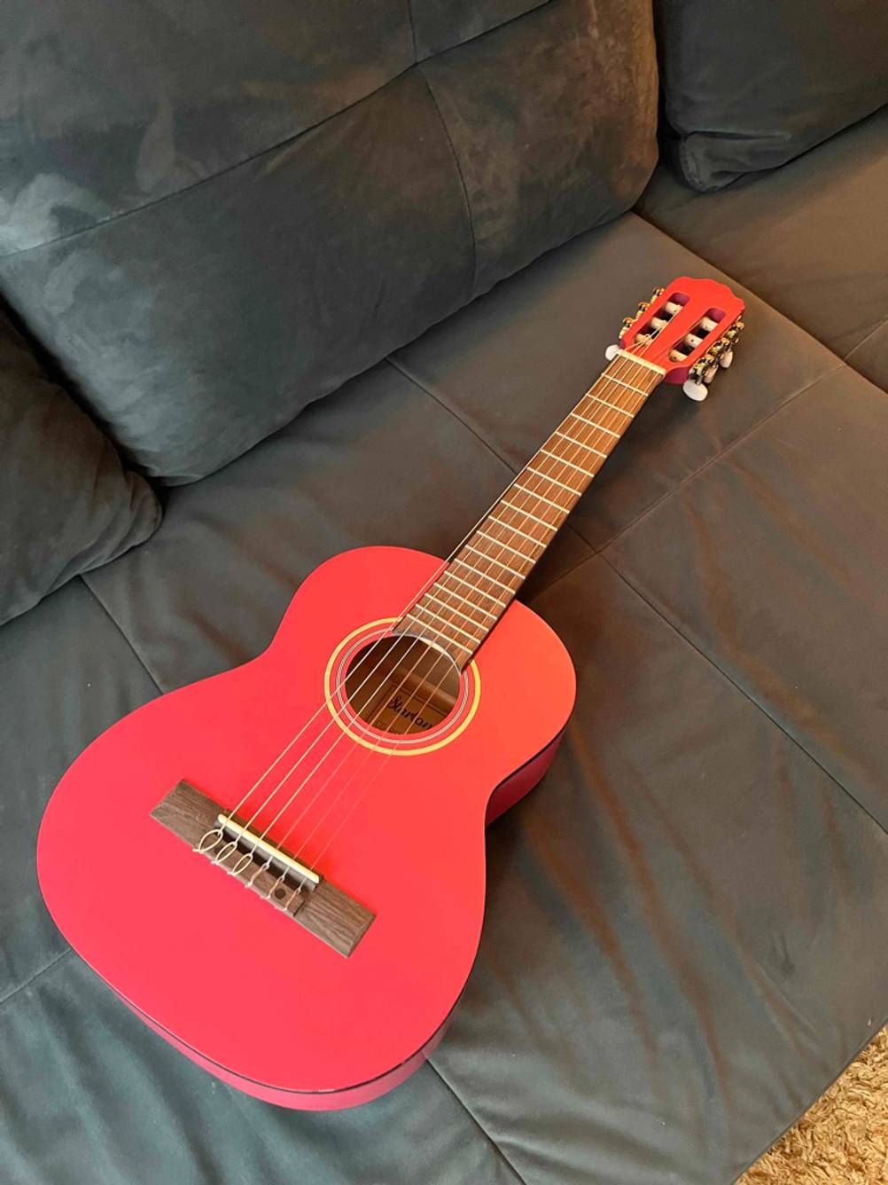 Eine getestete Kindergitarre liegt auf einem dunklen Sofa.