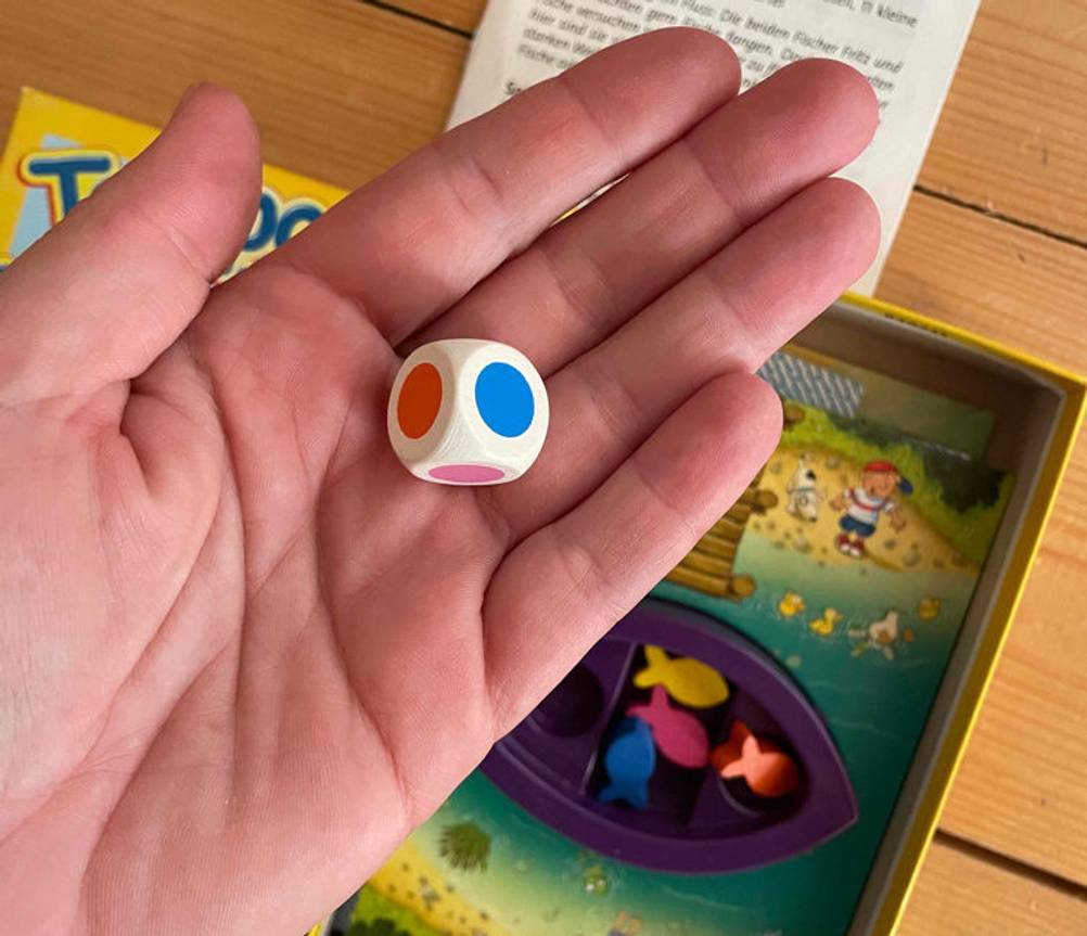 Würfelspiel im Test: ein Würfel mit bunten Punkten darauf wird über einem Würfelspiel gehalten.