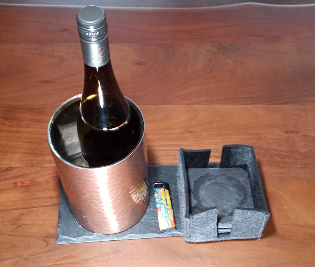 Im Test: Ein Weinkühler mit einer Flasche im Inneren steht neben Untersetzern auf einem Stein.