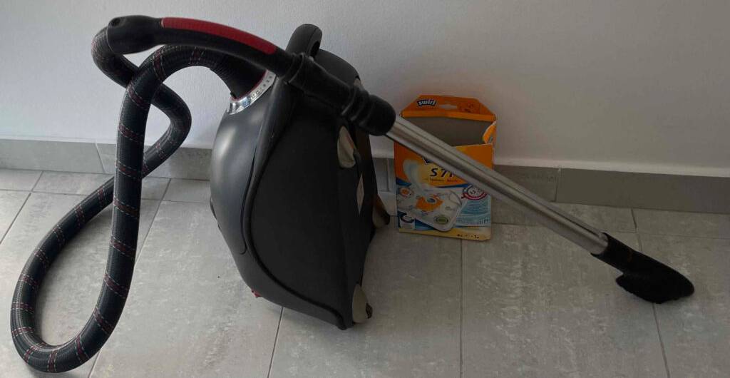 Ein schwarzer Staubsauger und eine Schachtel Beutel stehen vor einer hellen Wand