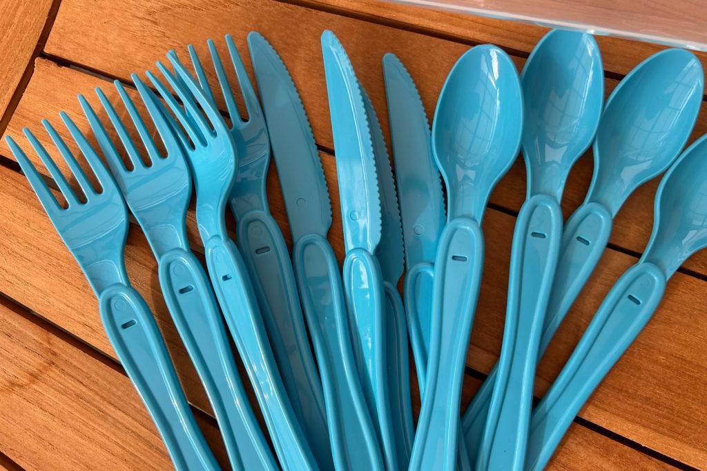 Blaue Campingmesser, Campinggabeln und Campinglöffel. auf einem Holzisch.