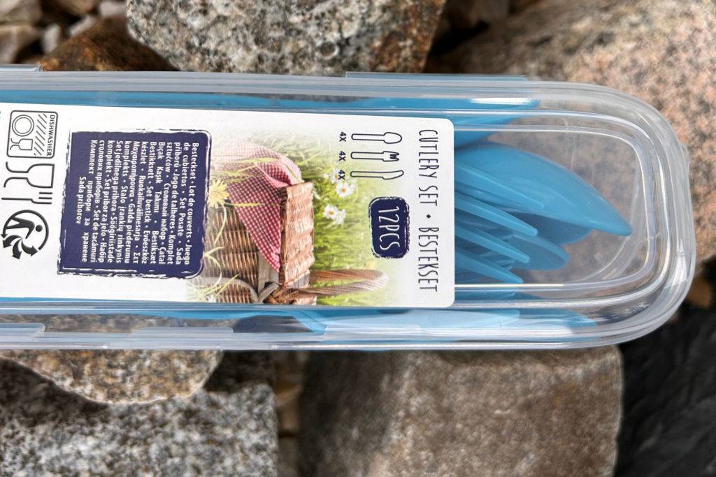 Blaues Campingbesteck in Box auf Steine gelegt.