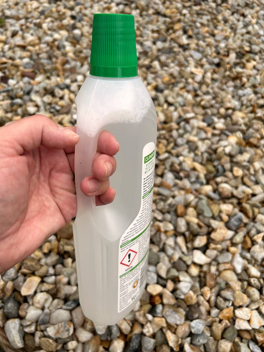 Eine Hand hält eine Flasche Steinreiniger am Henkel.