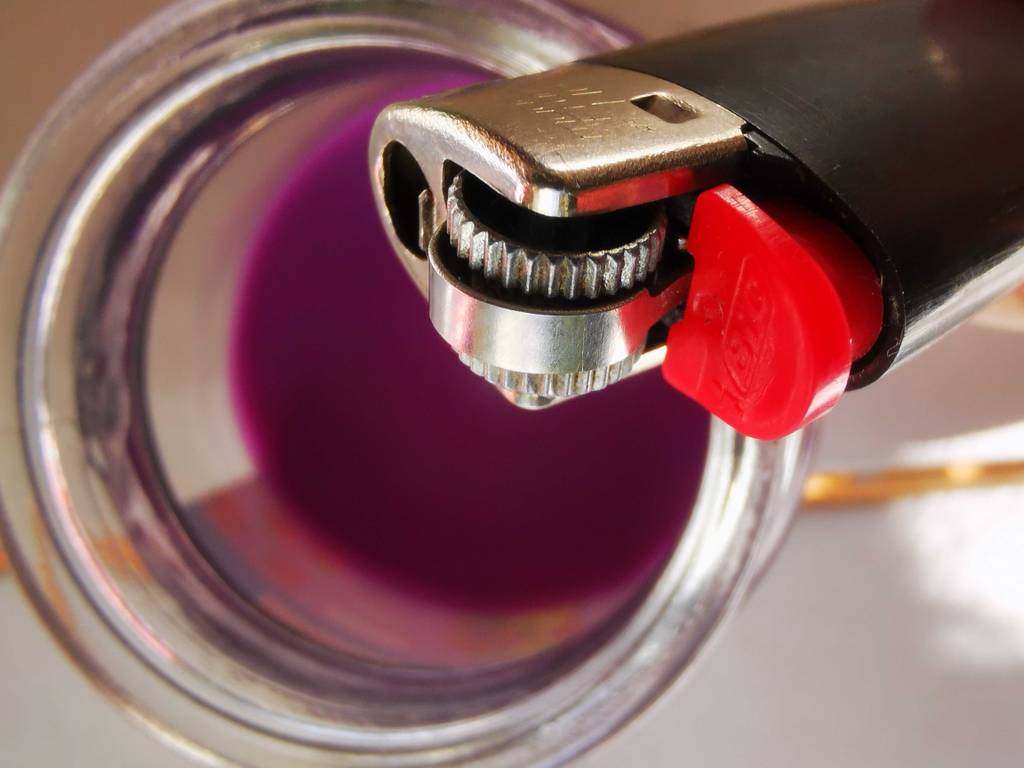 Nahaufnahme der Reibradzündung des getesteten Einwegfeuerzeugs, das sich über einer violetten Kerze Befindet.