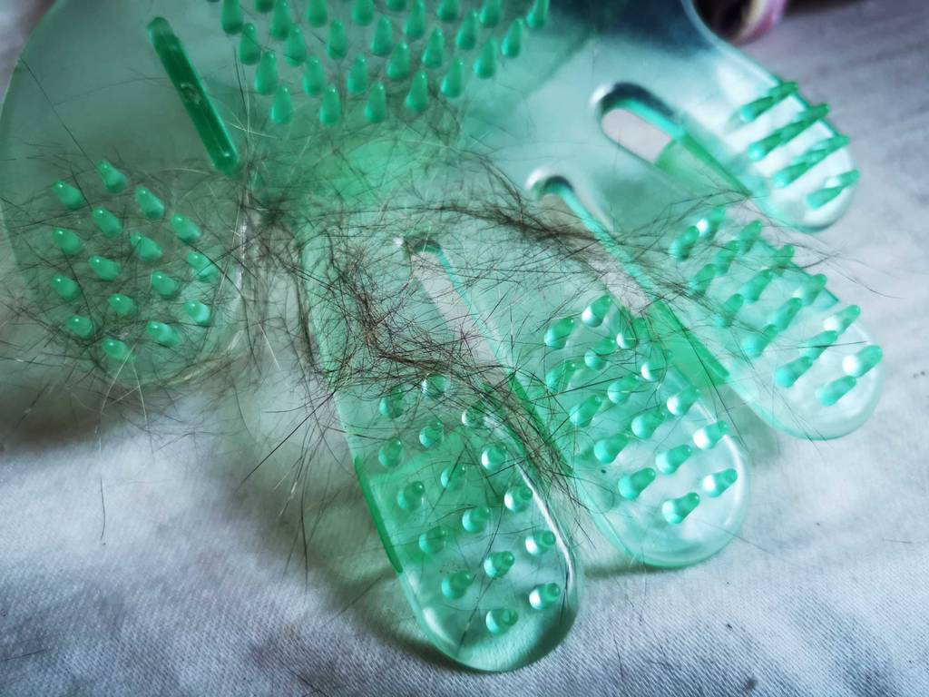 Im Test: Der Fellpflege-Handschuh mit Noppen liegt inklusive mehrerer Tierhaare auf einer weißen Oberfläche.