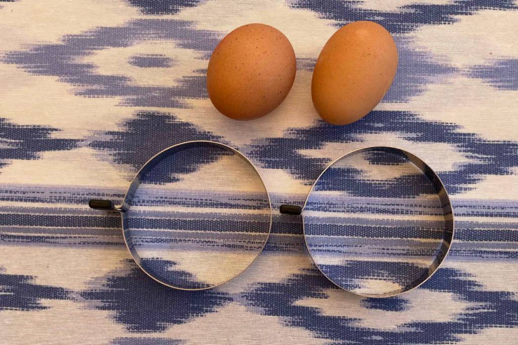 Zwei getestete Spiegeleiformen neben zwei Eiern auf einer blauweißen Tischdecke