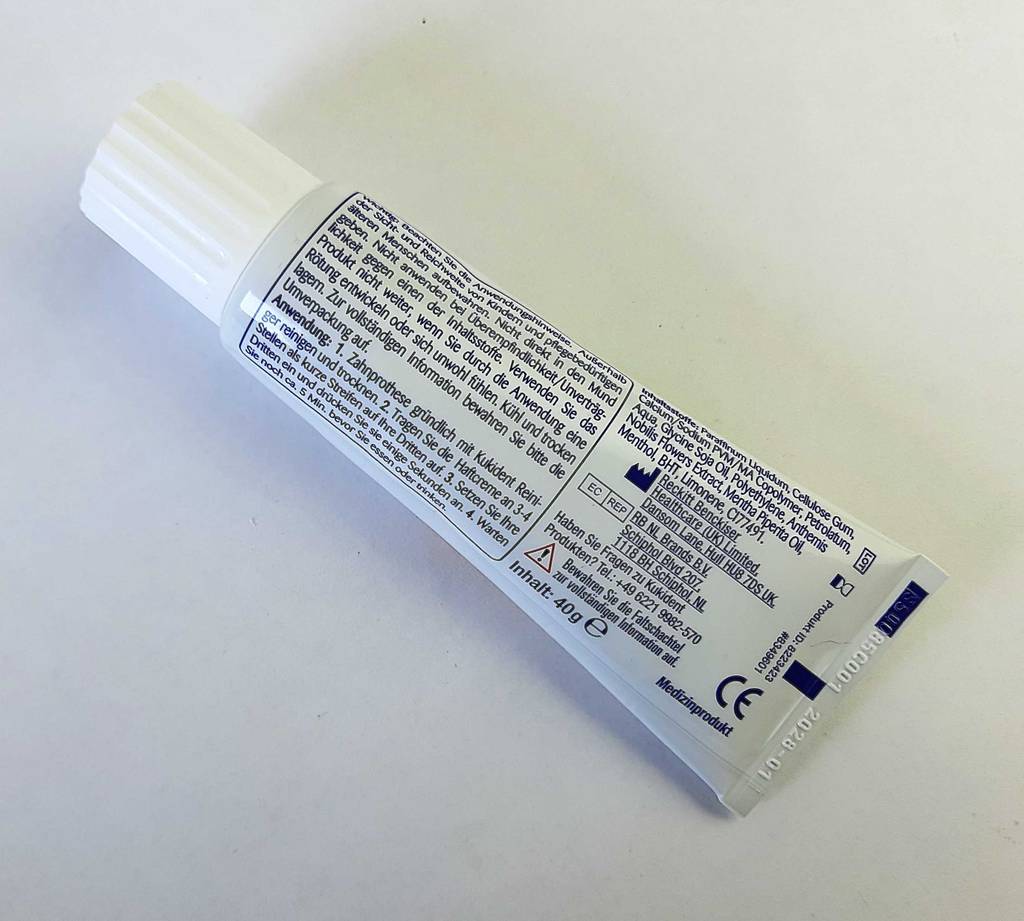 Die Haftcreme im Test liegt in der Tube mit Blick auf die Produkt- und Anwendungsangaben auf der weißen Oberfläche.