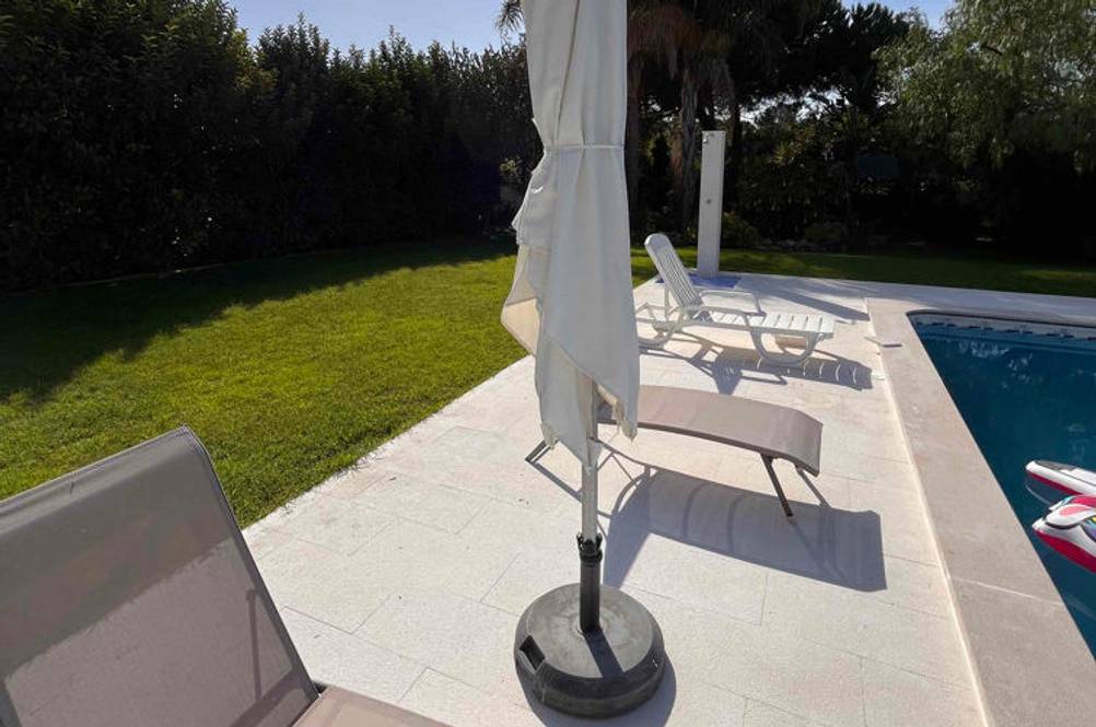 Sonnenschirm im Test: geschlossener Sonnenschirm in einem Garten neben Liegestühle und Pool.