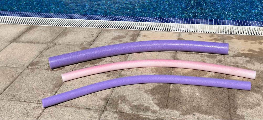 Drei getestete Schwimmnudeln liegen auf einem Fließenboden neben einem Pool