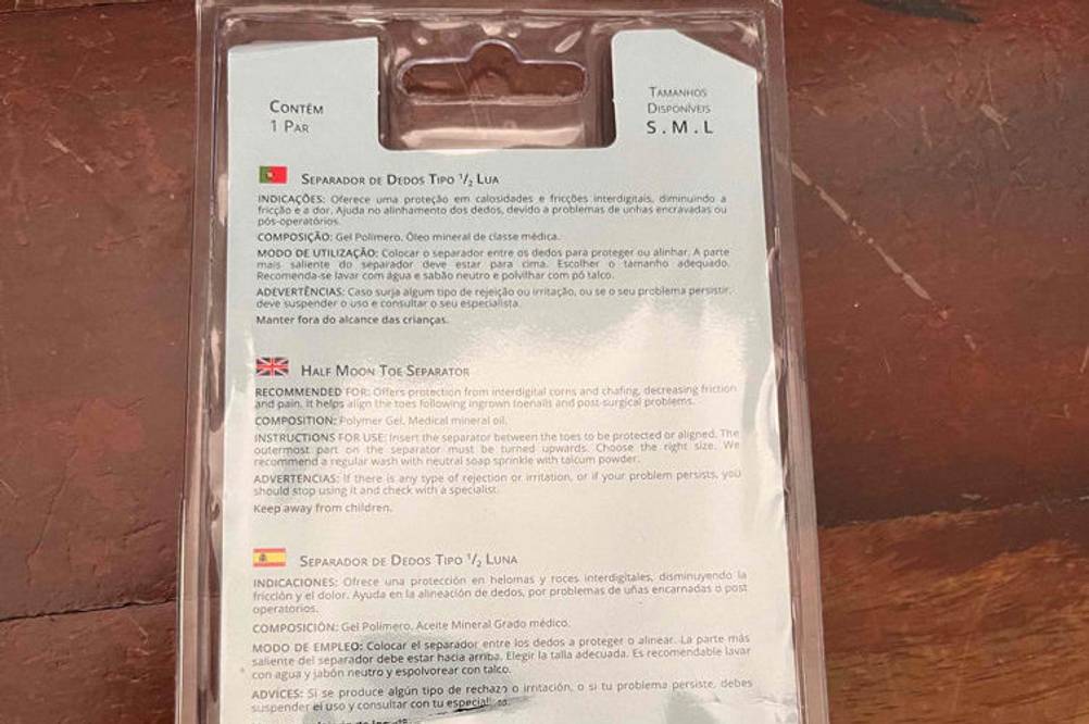 Zehenspreizer -Test: Rückseite der Verpackung von Zehenspreizer mit Beschreibung in verschiedenen Sprachen liegt auf einer Holzfläche.