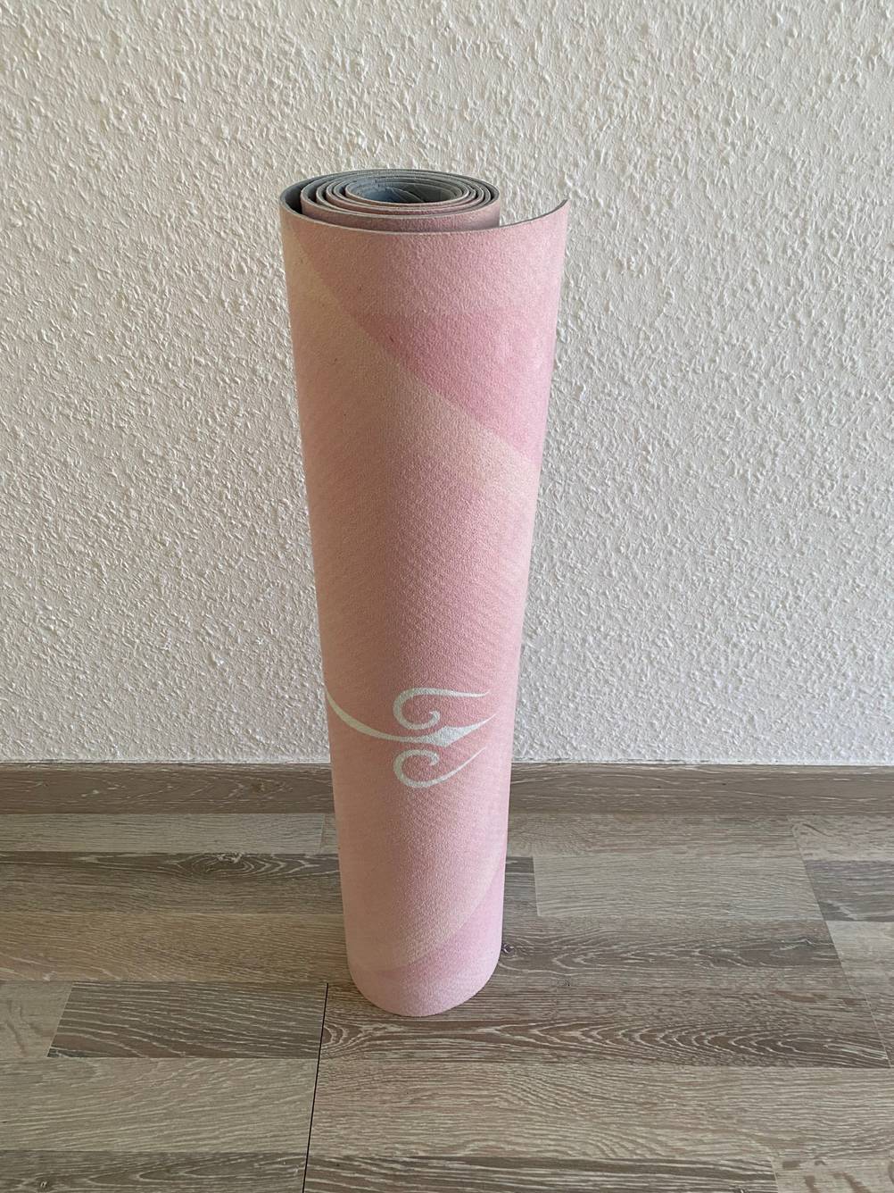 Yogamatte (Naturkautschuk) im Test: Eine Matte steht aufgerollt auf einem Holzboden vor einer hellen Wand