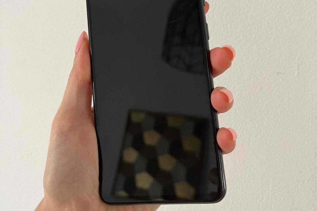 Günstiges Smartphone im Test: Eine Hand hält ein Smartphone mit Display nach vorne vor eine helle Wand