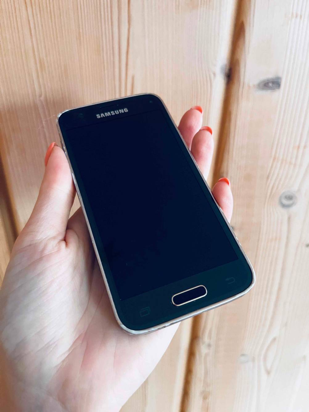 Im Test: Eine Hand hält die Vorderseite eines kleinen Smartphones vor eine Holzfläche.