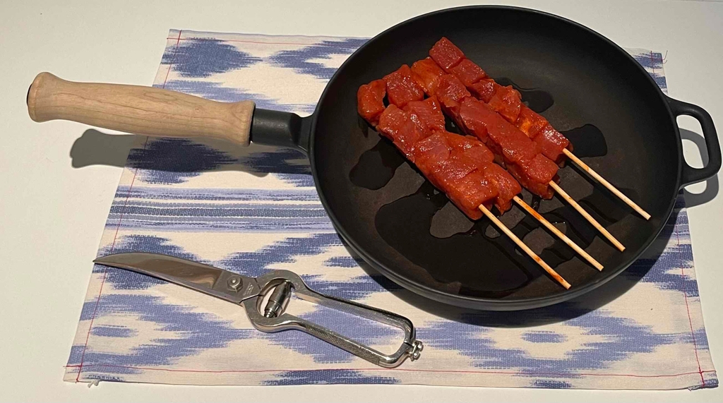 Getestete Geflügelschere liegt geschlossen auf einem Stoffset vor Pfanne mit Fleischstücken.