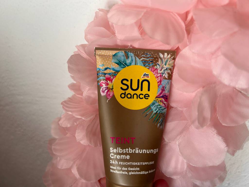 Gesichtsbräuner im Test: Tube vor einer rosa farbigen Trockenblume.