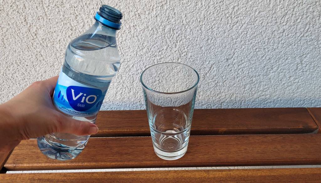 Stilles-Mineralwasser geöffnet und Glas daneben.