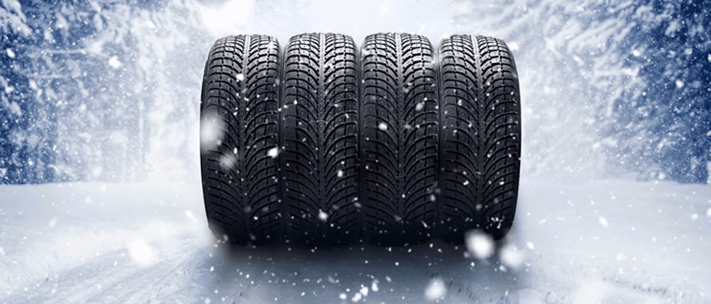 165/65-R14-Winterreifen im Test: Vier Reifen nebeneinander aufgestellt, im Hintergrund eine Winterlandschaft