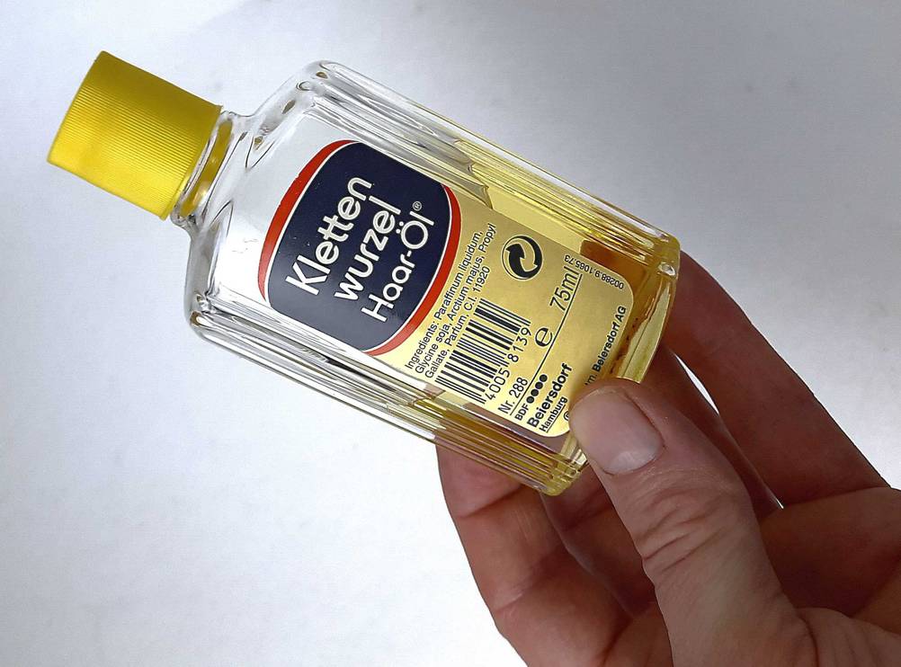 Das getestete Klettenwurzelöl für das Haar wird in der Hand gehalten.