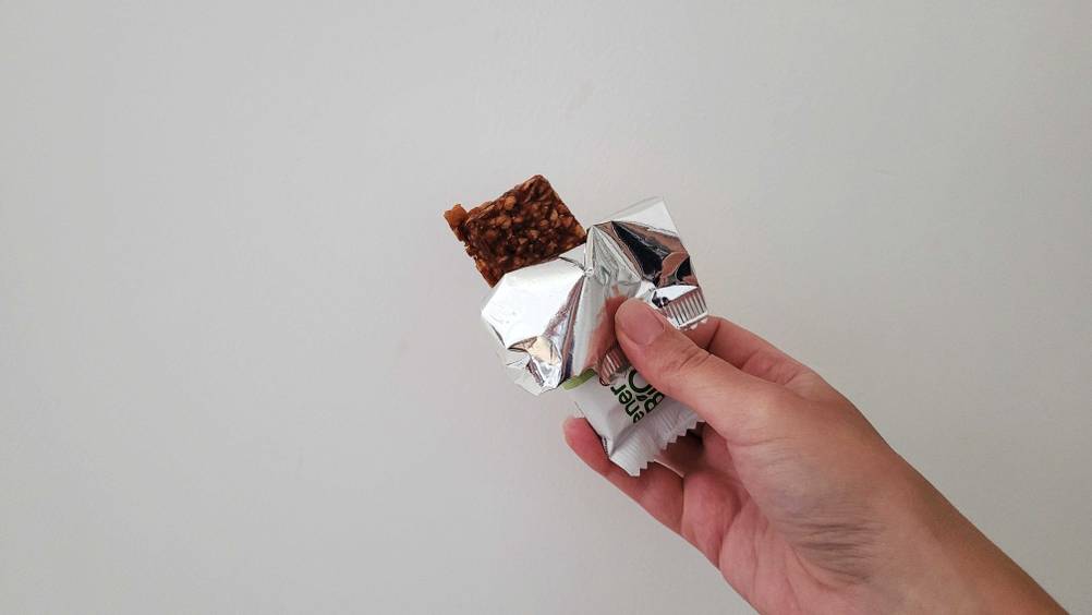 Fruchtriegel getestet: Eine Hand hält einen bis zur Hälte ausgepackten Riegel vor einen weißen Hintergrund.