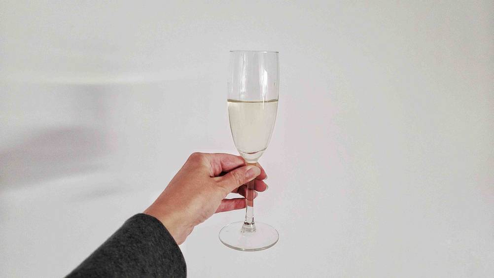 Sekt im Test: Eine Hand hält ein gefülltes Sektglas vor eine helle Wand