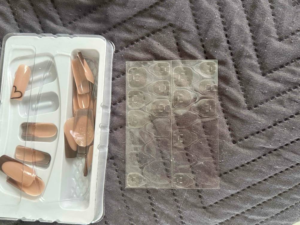 künstliche Fingernägel befinden sich noch in Verpackung und daneben durchsichtige Folie platziert.