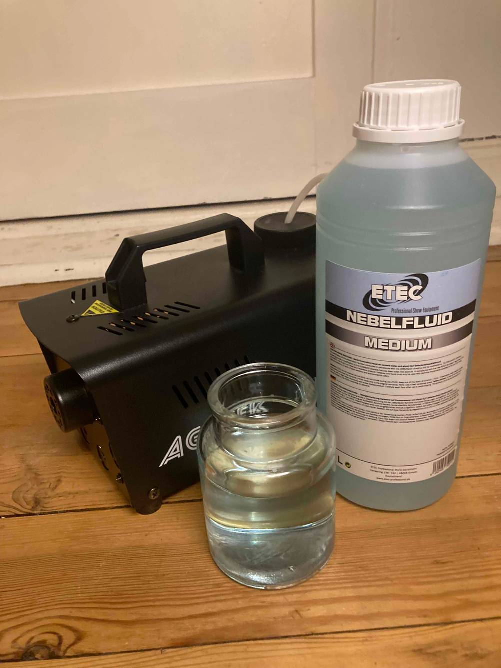 Nebelfluid-Test: ein Nebelfluid steht neben einer Nebelmaschine und einem Gefäß mit einer Flüssigkeit darin.
