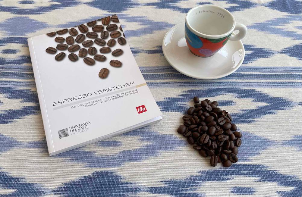 Espressobohnen getestet: Ein Buch über Espresso eine Tasse und Bohnen auf einer blauweißen Tischdecke