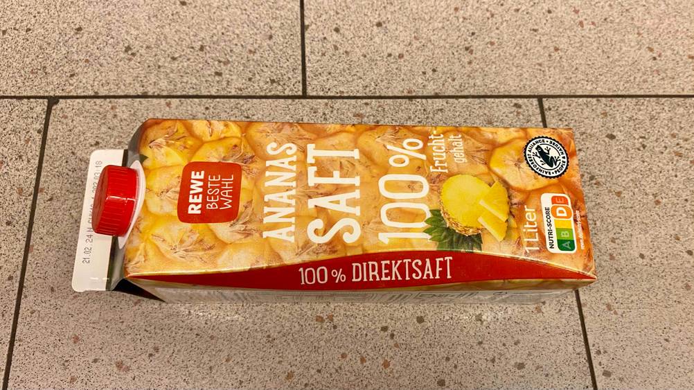 Eine Packung des getesteten Ananassaftes liegt horizontal auf einer Fließenoberfläche.