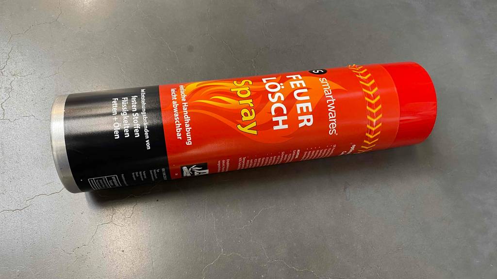 Eine getestete Dose Feuerlöschspray liegt horizontal auf einer grauen Fläche