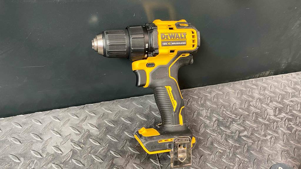 Ein gelber DeWalt-Akku-Bohrschrauber im Test lehnt vor einer anthrazitfarbenen Wand auf einem grauen Metallregal im Verkaufsbereich.
