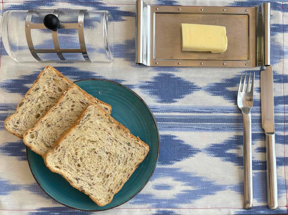 Butterdose im Test: Ein Teller mit Toast, Besteck und eine geöffnete Butterdose neben ihrem Deckel auf einer Tischdecke