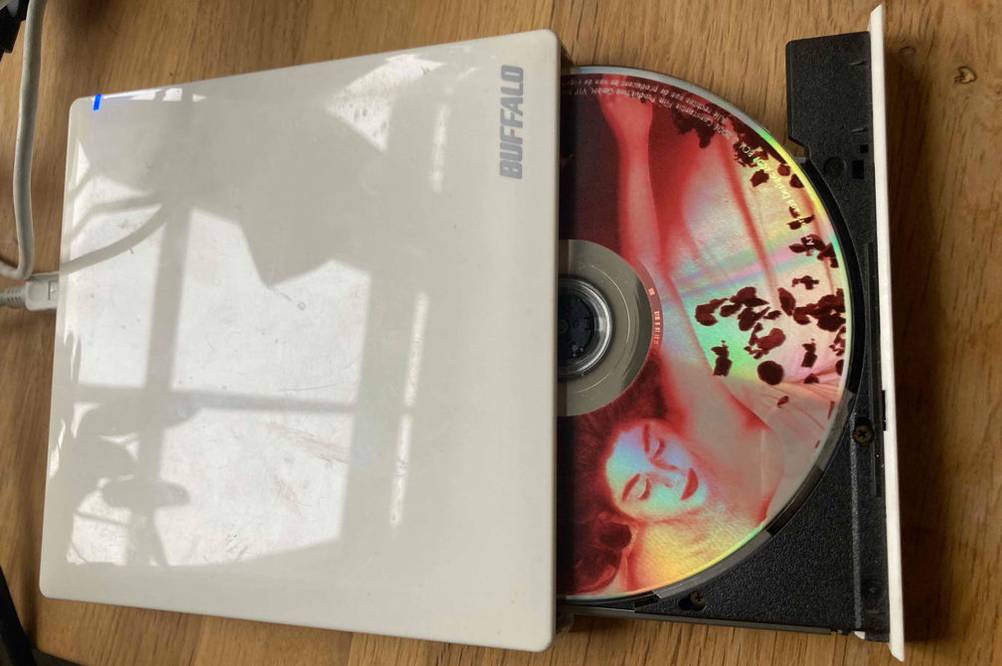 Ein getestetes Externes DVD-Laufwerk mit geöffneter Lade und einer DVD darin auf einer Holfläche.