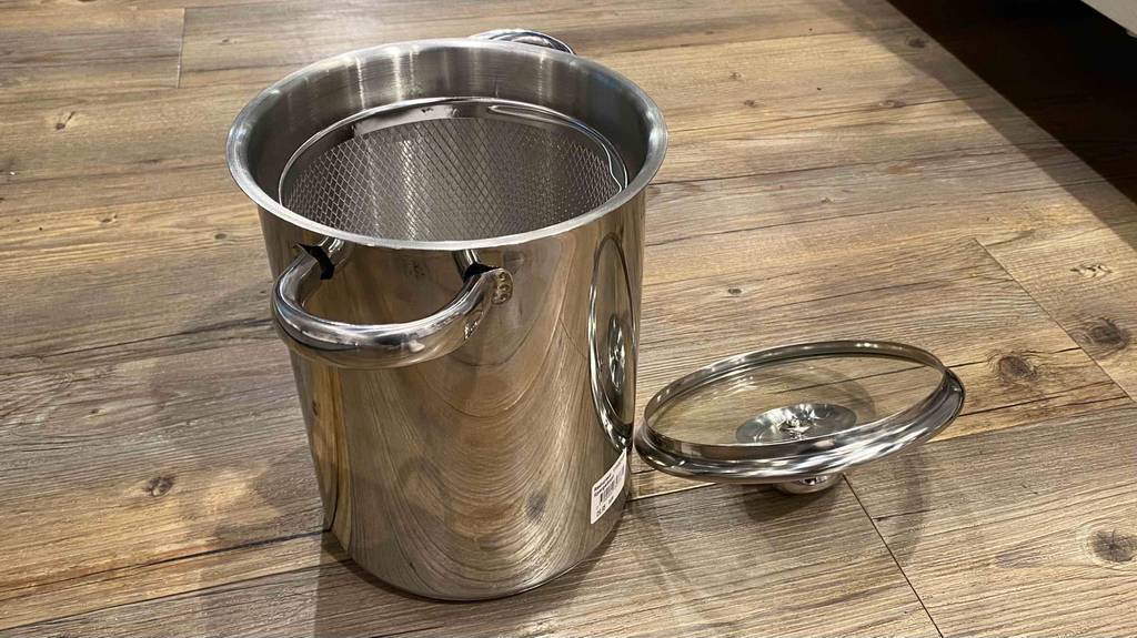 Neben einem getesteten Spargeltopf liegt sein Deckel auf einer Holzfläche.