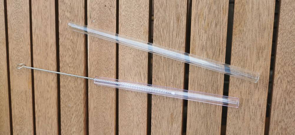 Glas-Strohhalme im Test: zwei durchsichtige Glas-Strohhalme mit einer Reinigungsbürste darin auf einem Holztisch.